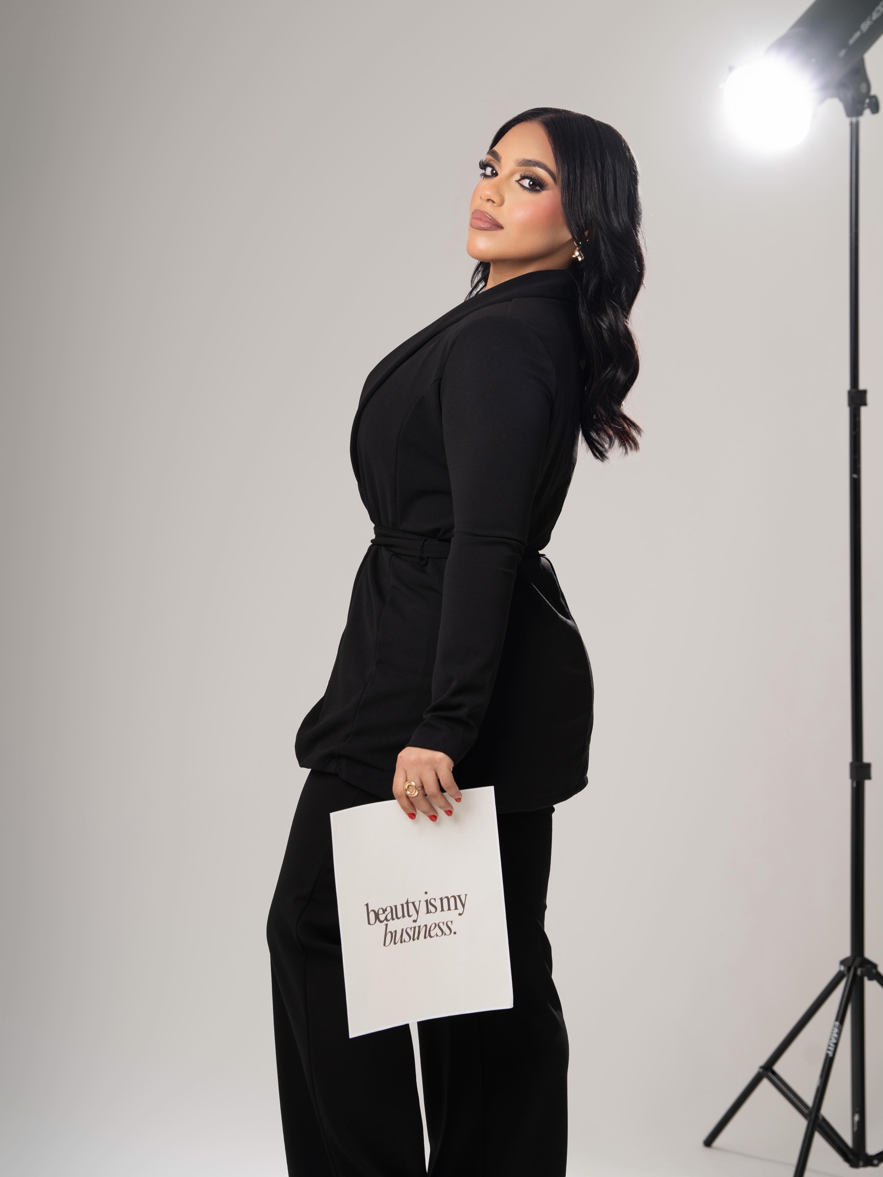 Alondra Krystal con traje negro sosteniendo un letrero que dice beauty is my business